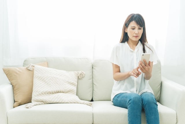 リビングでスマホを心配げに眺めている50代女性